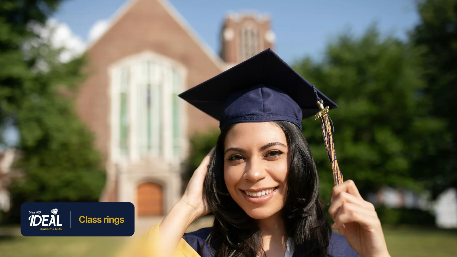 A smiling graduate in a navy cap and gown outside a brick campus building